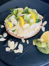 a black plate with kiwi, lemon and almonds on it